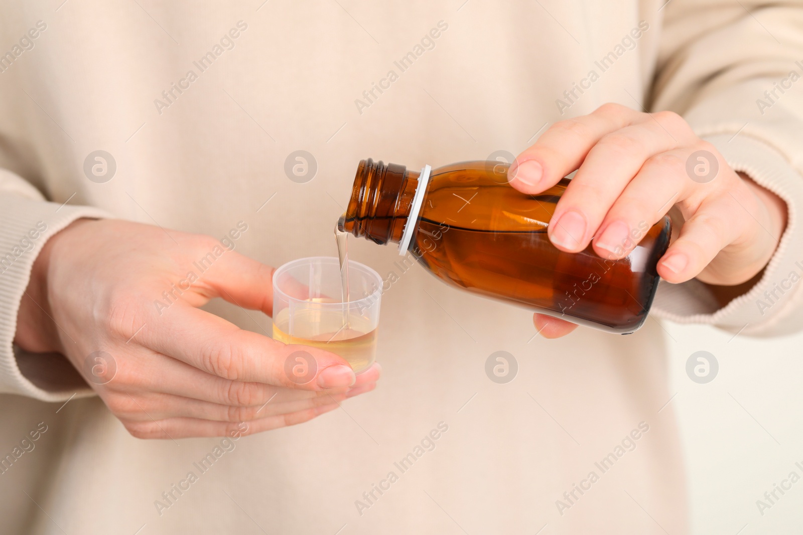 Photo of Woman pouring syrup from bottle into measuring cup, closeup. Cold medicine