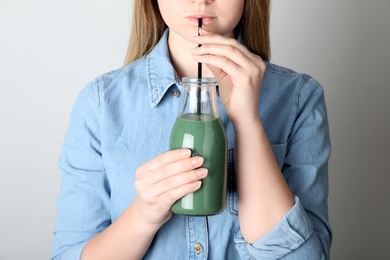 Woman drinking spirulina smoothie from bottle on grey background, closeup