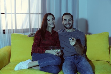 Photo of Happy young couple watching TV on sofa at home