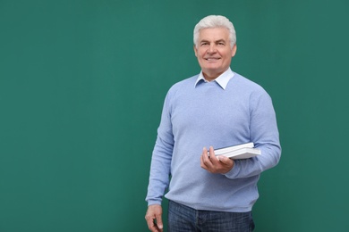 Photo of Portrait of senior teacher with books at green chalkboard, space for text
