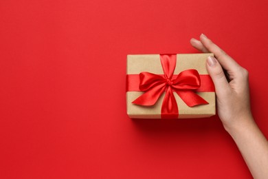 Photo of Woman holding beautiful gift box on red background, top view. Space for text
