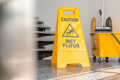 Photo of Safety sign with phrase Caution wet floor and mop bucket near stairs. Cleaning service