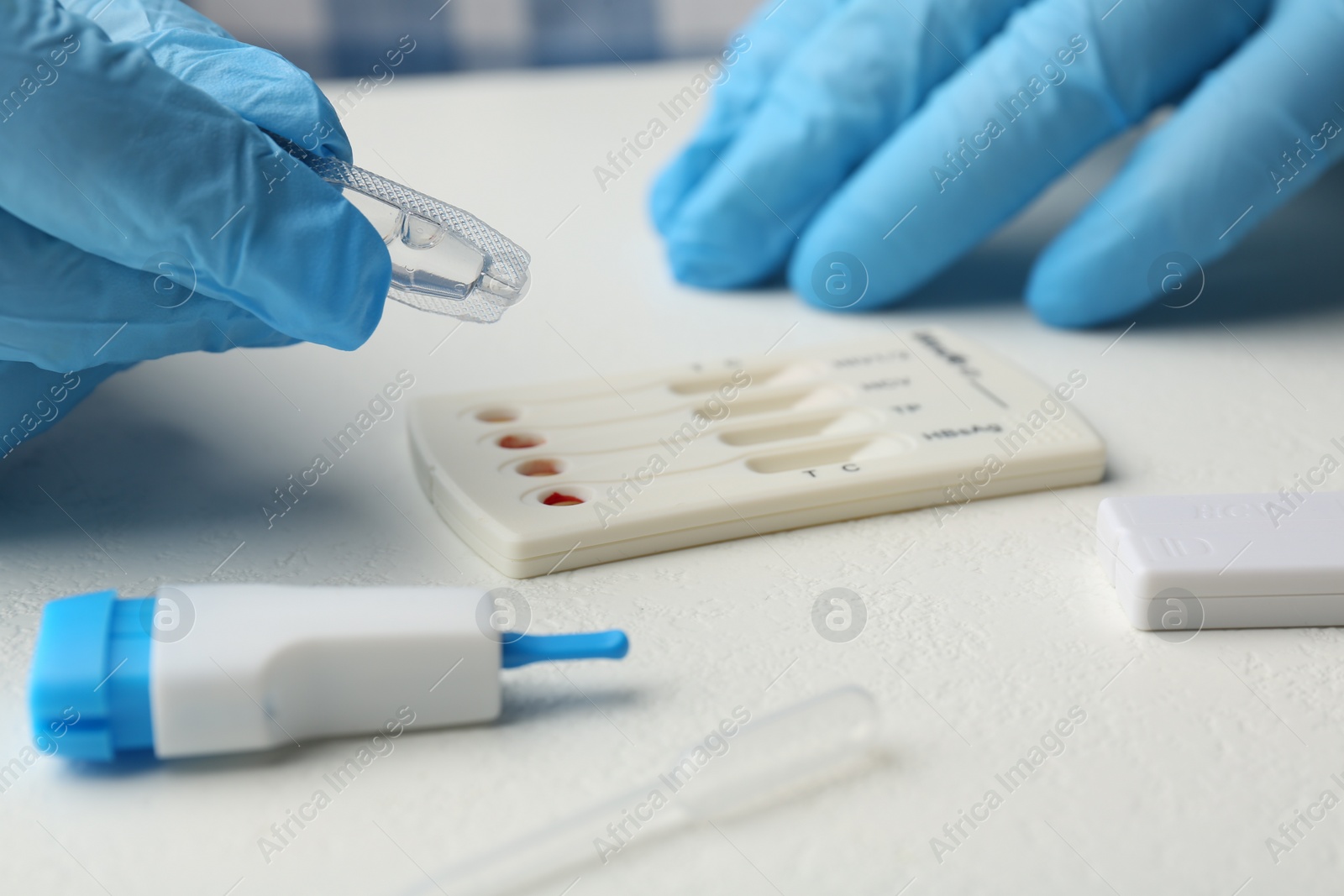 Photo of Doctor dropping buffer solution onto disposable multi-infection express test cassette at white table, closeup