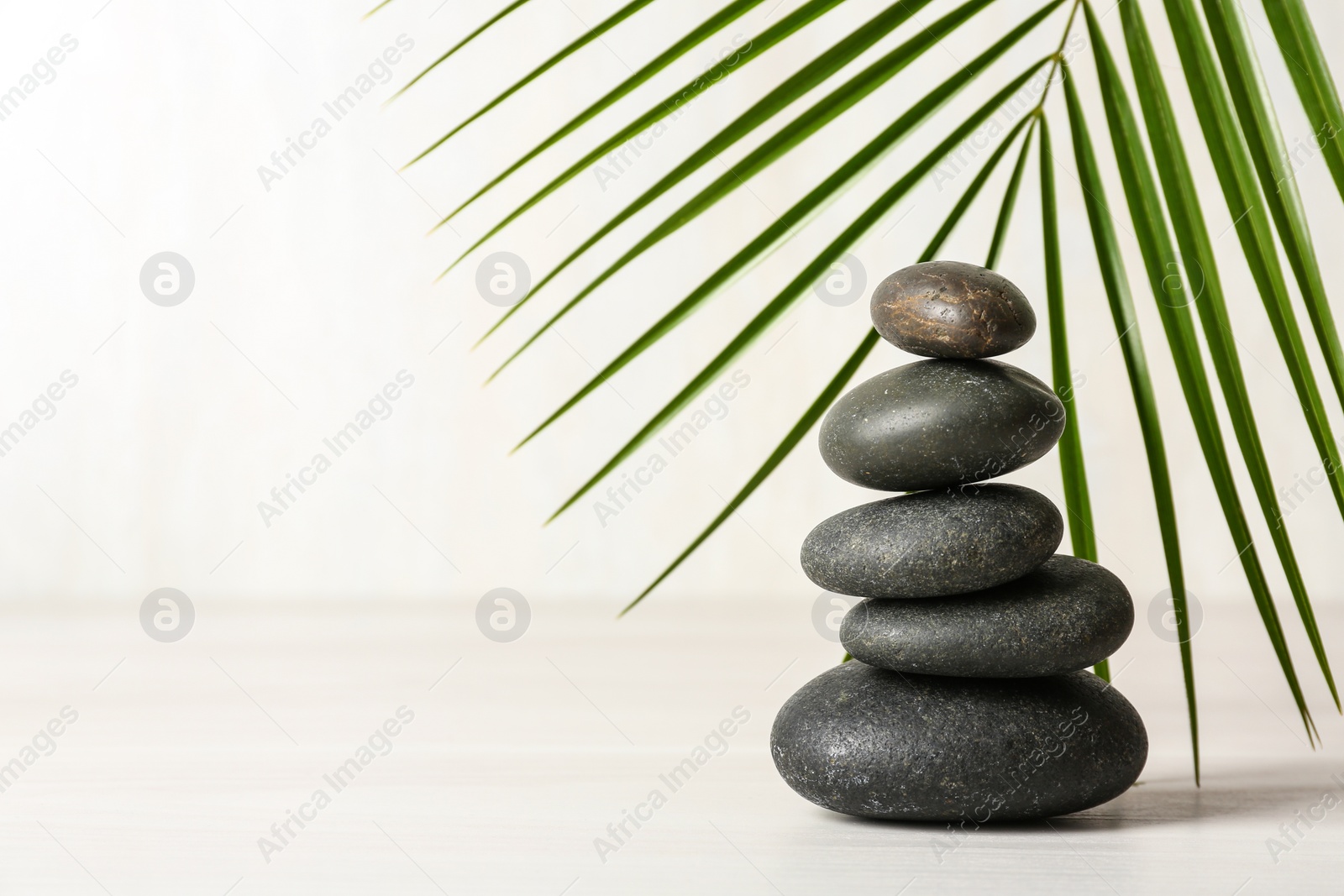 Photo of Stack of spa stones and palm leaf on table against white background, space for text