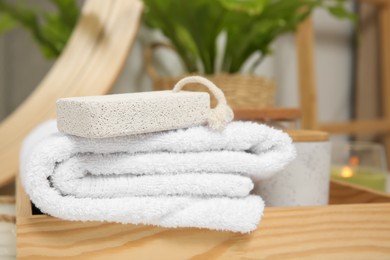 Photo of Pumice stone and white towel on wooden tray indoors, closeup