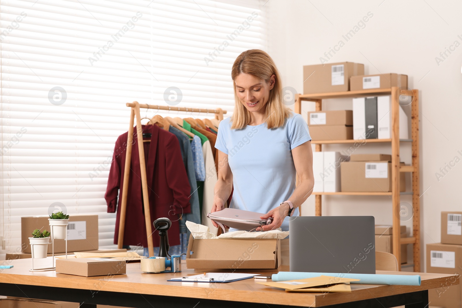 Photo of Seller packing bag into cardboard box at table in office. Online store