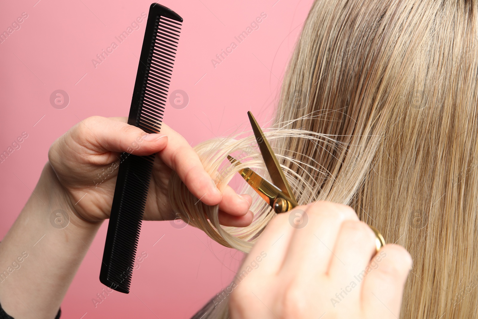 Photo of Hairdresser cutting client's hair with scissors on pink background, closeup