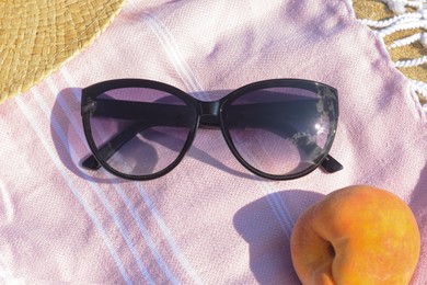 Photo of Beautiful sunglasses and peach on blanket, closeup