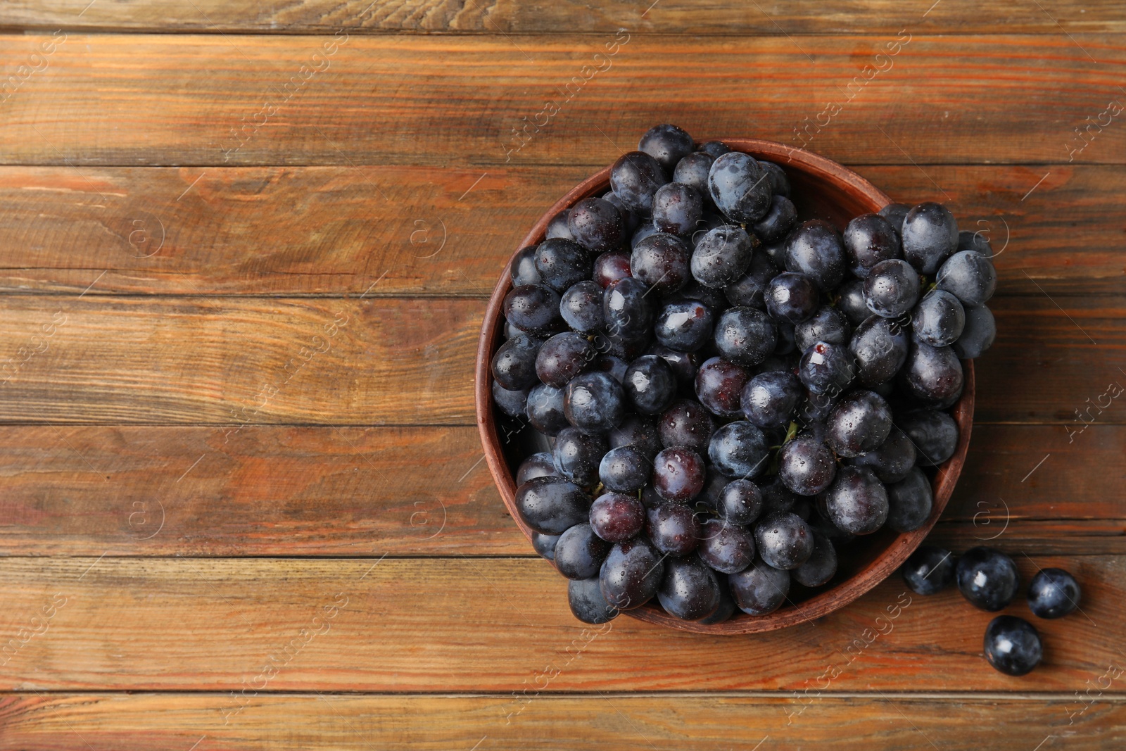 Photo of Fresh ripe juicy grapes in bowl and space for text on wooden background, top view