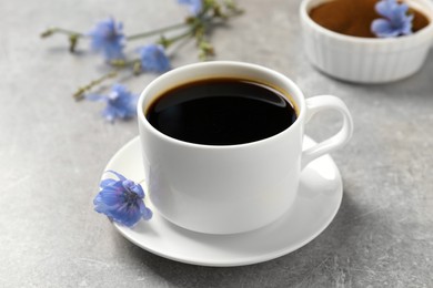 Photo of Cup of delicious chicory drink and flowers on light grey table, closeup