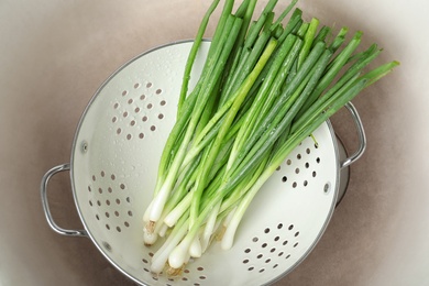 Photo of Colander with bunch of fresh green onions in kitchen sink