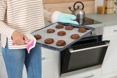 Photo of Young woman with tray of oven baked cookies in kitchen, closeup