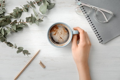 Photo of Young woman with cup of delicious hot coffee at table, top view