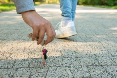 Man picking lost keys from ground, closeup. Space for text