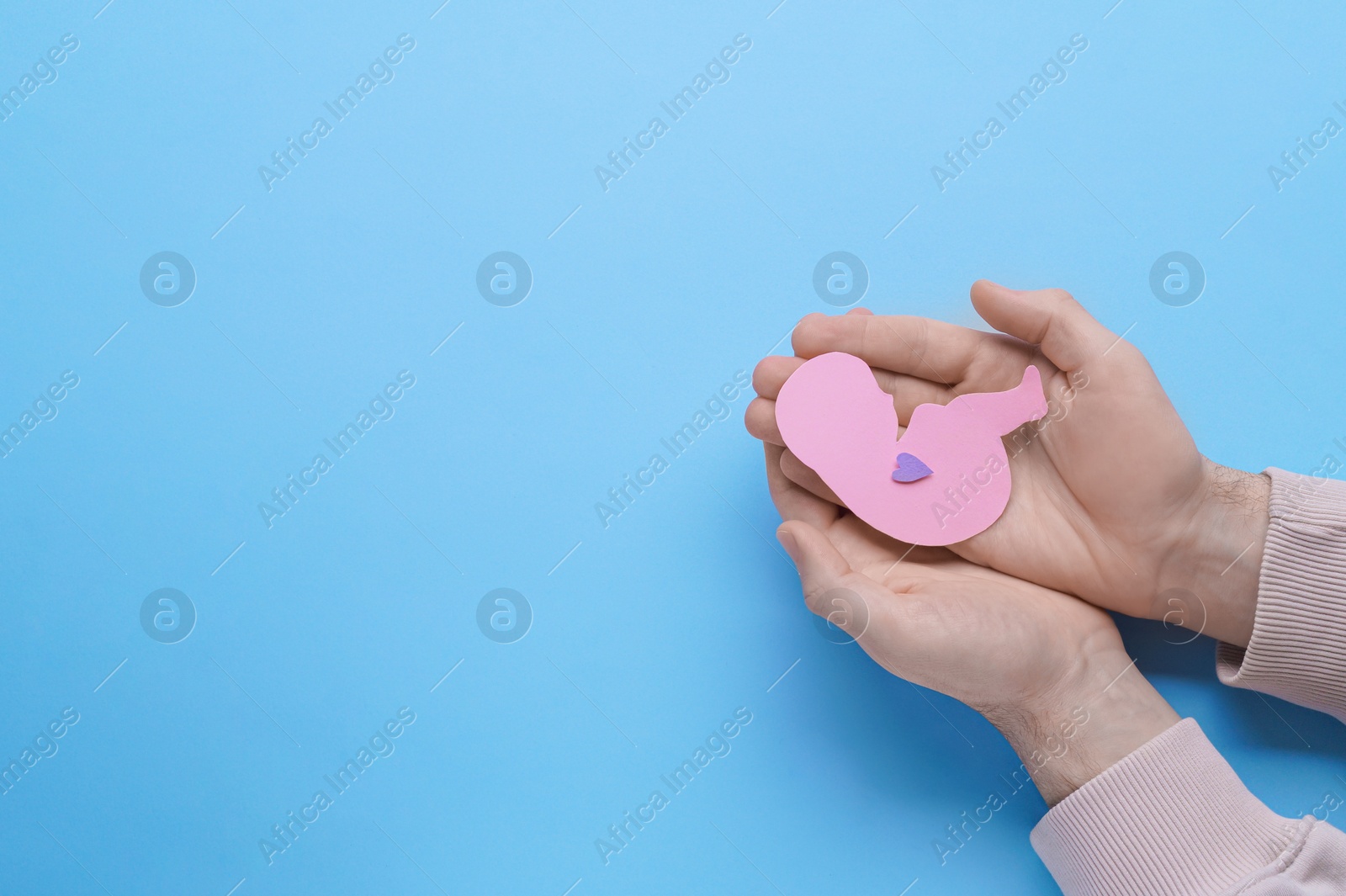 Photo of Female health. Man holding newborn paper figure on light blue background, top view with space for text