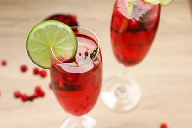 Tasty cranberry cocktail with rosemary and lime in glasses on beige table, closeup