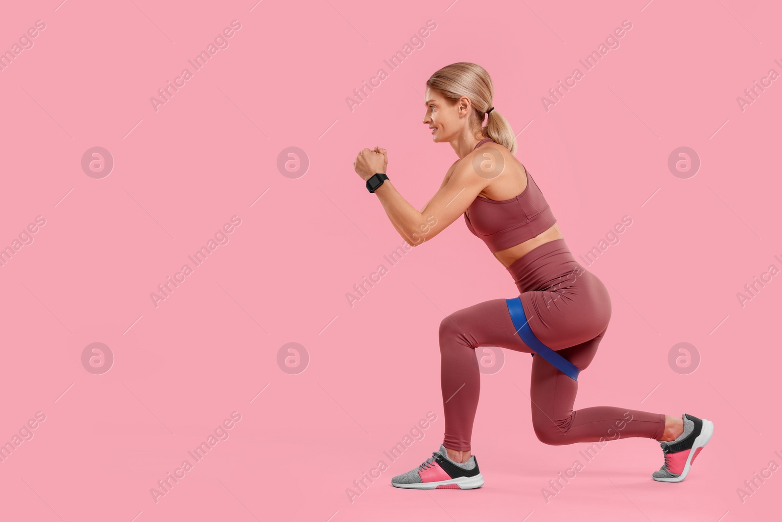 Photo of Woman exercising with elastic resistance band on pink background. Space for text