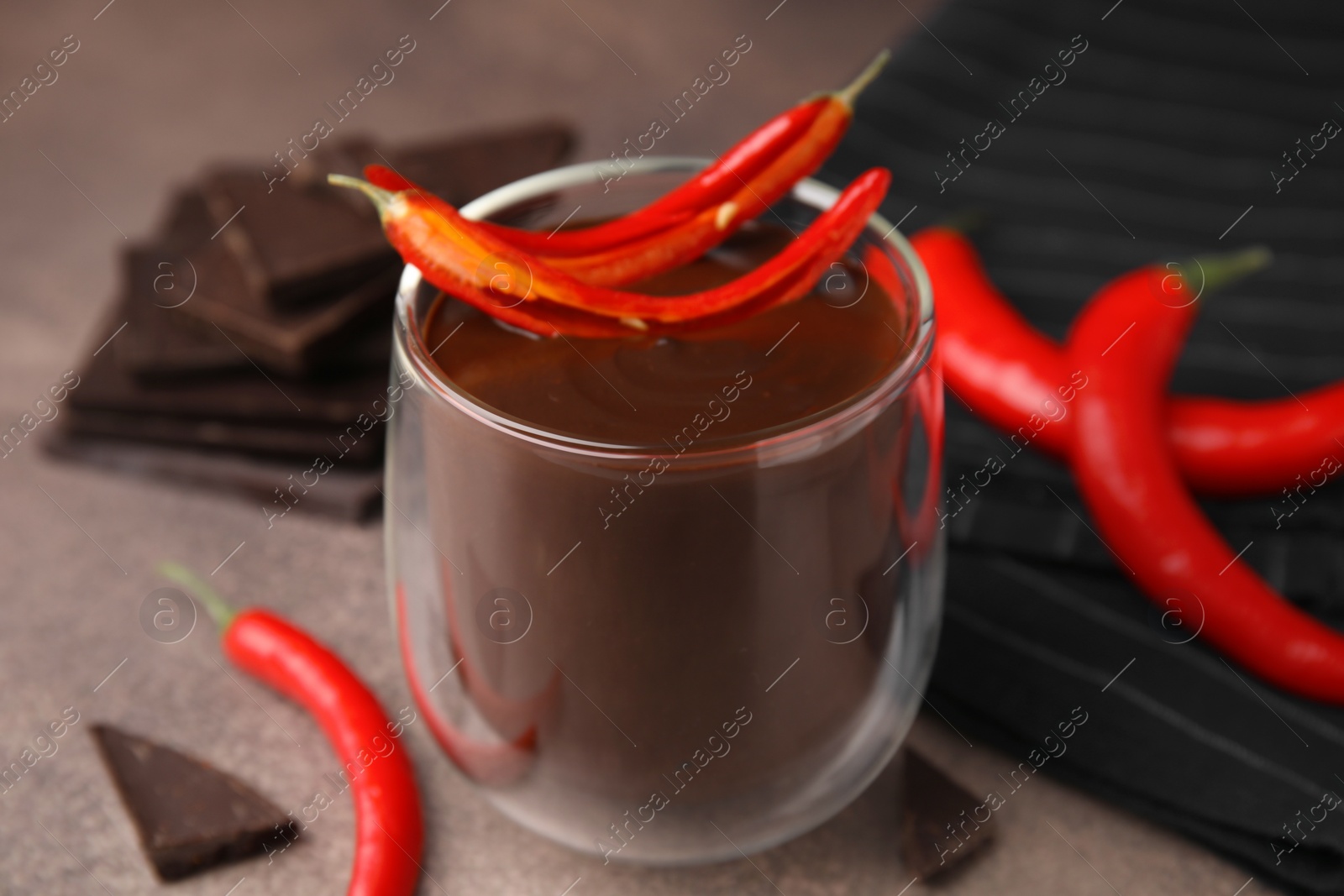 Photo of Delicious hot chocolate with chili peppers on brown textured table, closeup