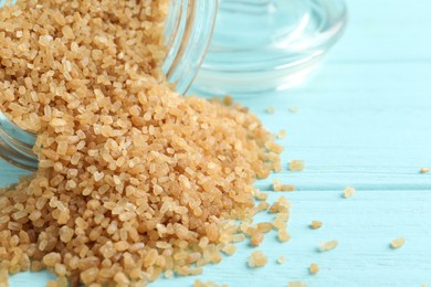 Photo of Overturned bowl of brown sugar on light blue wooden table, closeup