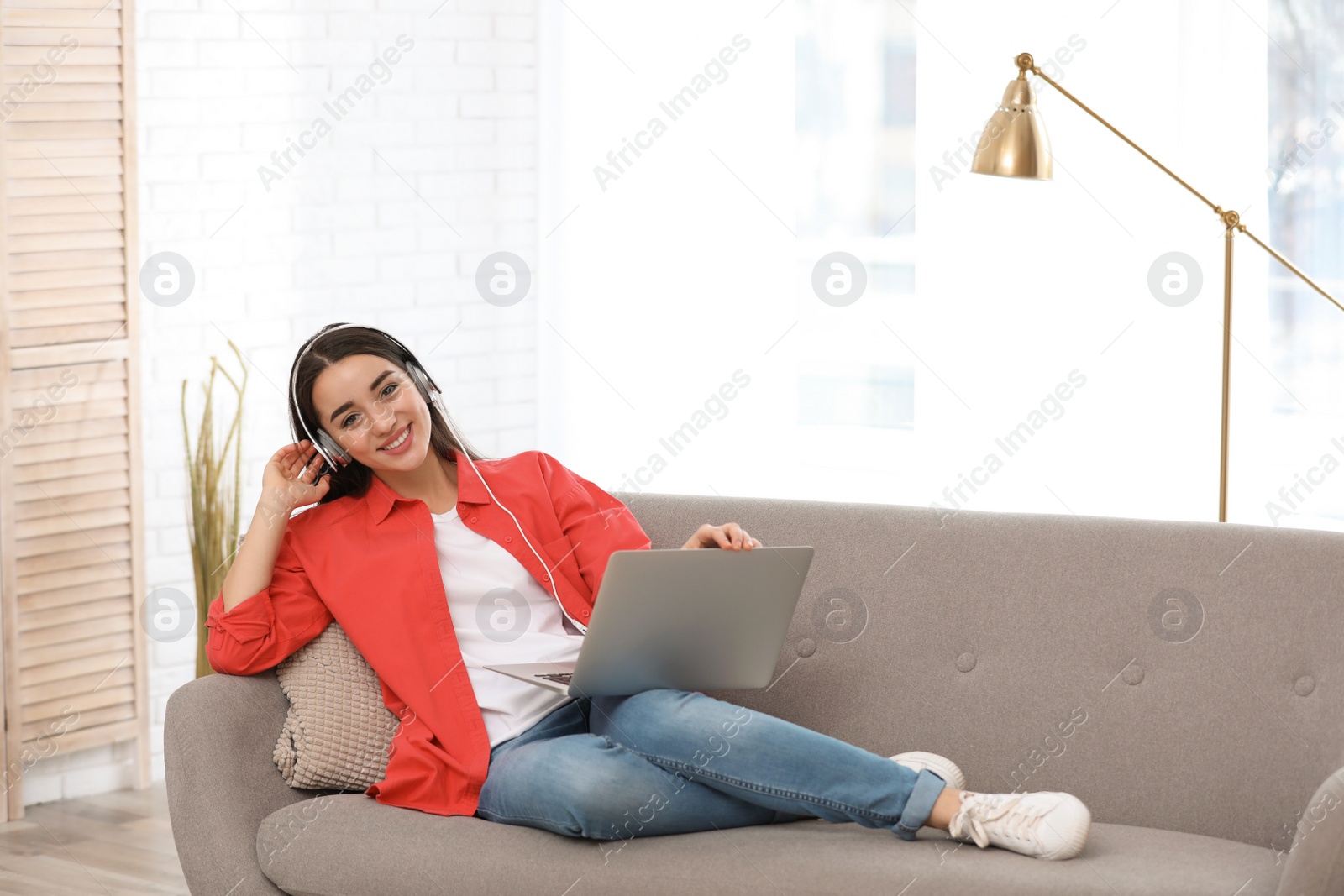 Photo of Young woman with headphones and laptop on sofa in living room