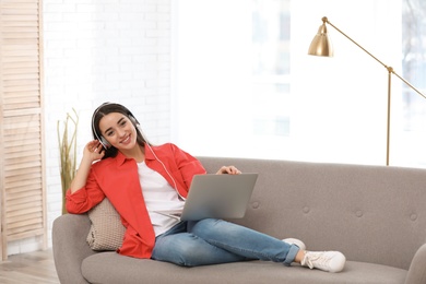 Young woman with headphones and laptop on sofa in living room