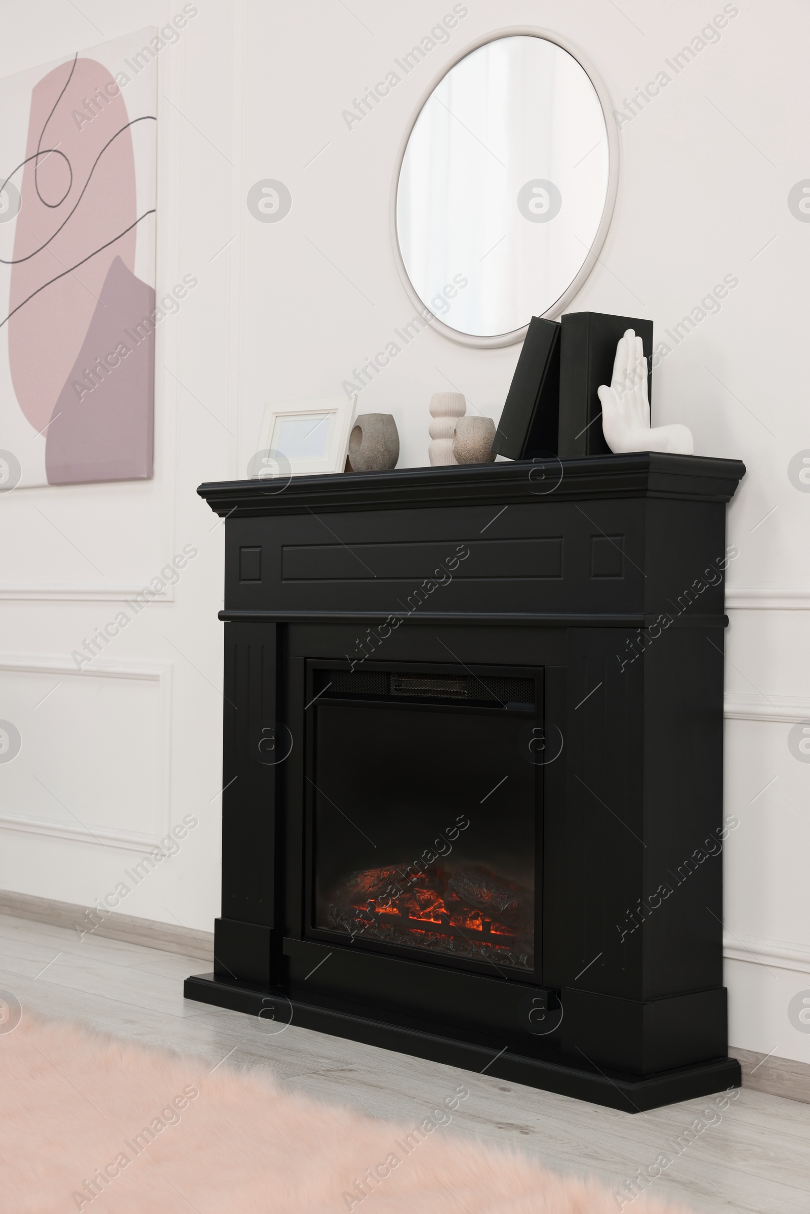 Photo of Black stylish fireplace with accessories under round mirror in cosy living room