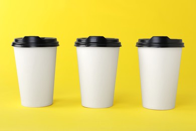 Paper cups with black lids on yellow background. Coffee to go