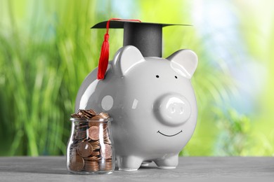 Photo of Scholarship concept. Glass jar with coins, piggy bank and graduation cap on grey table
