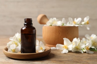 Jasmine essential oil and fresh flowers on wooden table, space for text