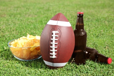 Photo of Ball with beverage and chips on fresh green field grass. American football match