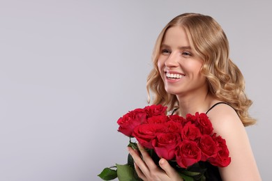 Beautiful woman with blonde hair holding bouquet of red roses on light grey background. Space for text