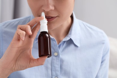 Woman using nasal spray on blurred background, closeup. Space for text