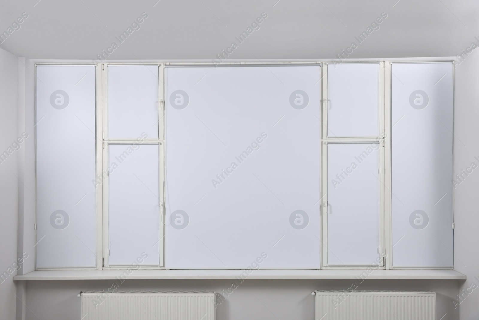 Photo of Large window with closed white roller blinds indoors