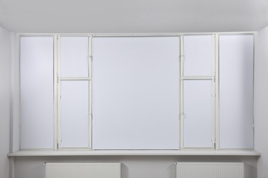 Photo of Large window with closed white roller blinds indoors