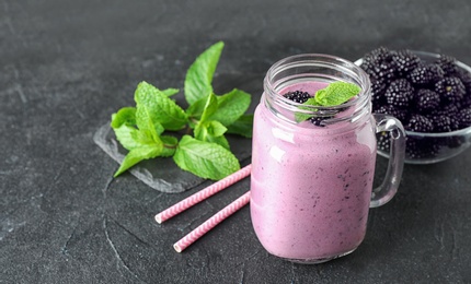 Photo of Delicious blackberry smoothie in mason jar on black table. Space for text
