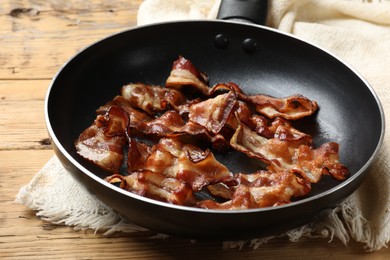 Delicious bacon slices in frying pan on wooden table, closeup