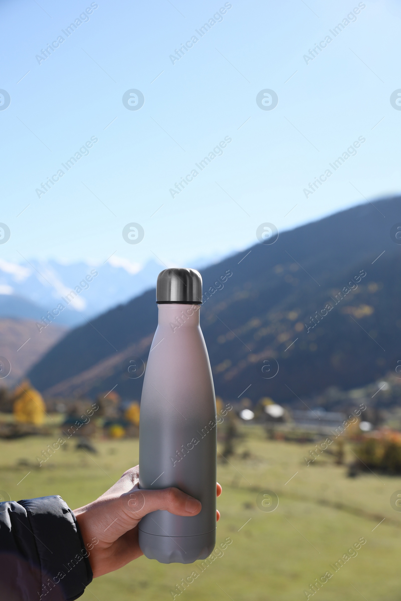 Photo of Boy holding thermo bottle with drink in mountains on sunny day, closeup