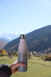 Photo of Boy holding thermo bottle with drink in mountains on sunny day, closeup