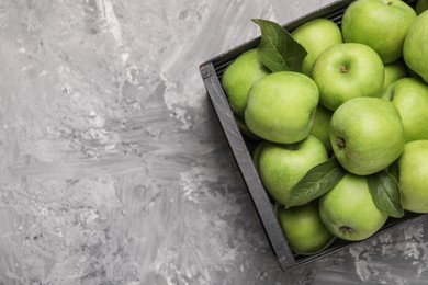 Fresh green apples in crate on grey textured table, top view. Space for text