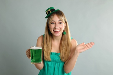 Photo of Happy woman in St Patrick's Day outfit with beer on light grey background