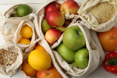 Cotton eco bags with fruits and cereals on white wooden table, top view