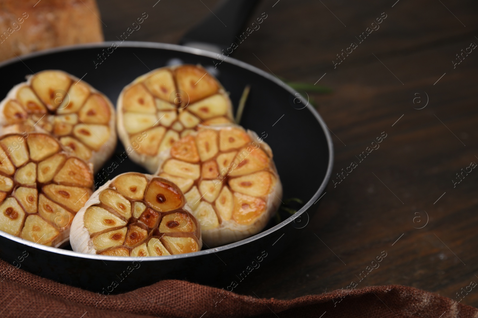 Photo of Frying pan with fried garlic on wooden table, closeup. Space for text