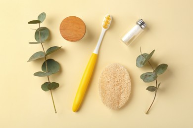 Plastic toothbrush, eucalyptus branches and other toiletries on pale yellow background, flat lay