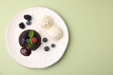Photo of Plate with delicious chocolate fondant, berries, mint and ice cream on light green table, top view. Space for text