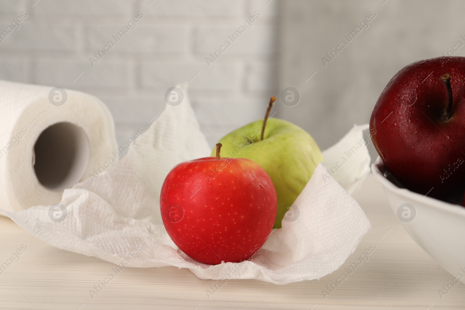 Photo of Fresh apples and paper towel on light wooden table