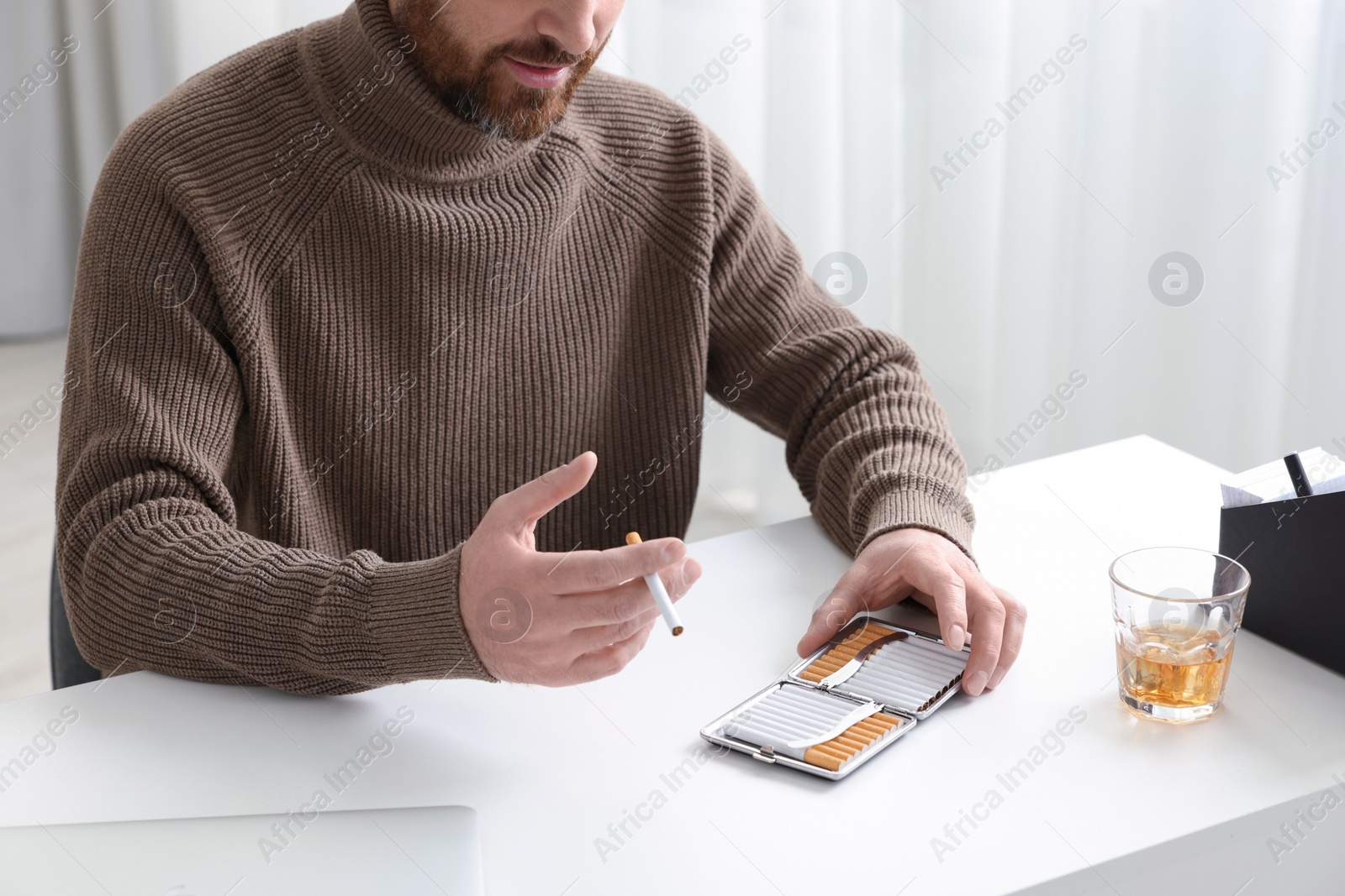 Photo of Man taking cigarette from case at white table in office, closeup