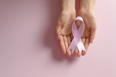 Woman holding pink ribbon on color background, top view with space for text. Breast cancer awareness