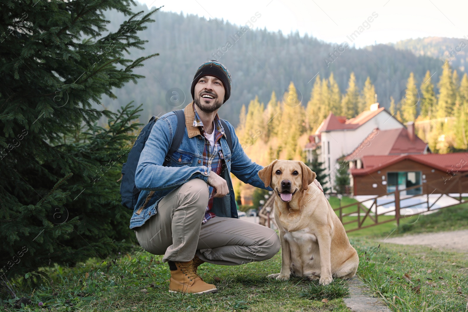 Photo of Happy man and adorable dog sitting on green grass in mountains. Traveling with pet