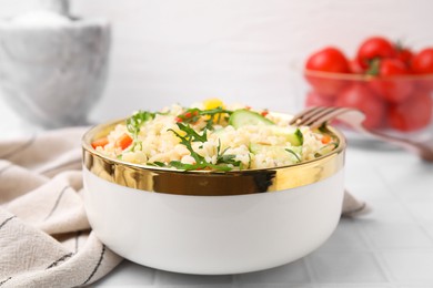 Cooked bulgur with vegetables in bowl on white tiled table, closeup