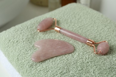 Photo of Rose quartz gua sha tool and natural face roller on towel, closeup